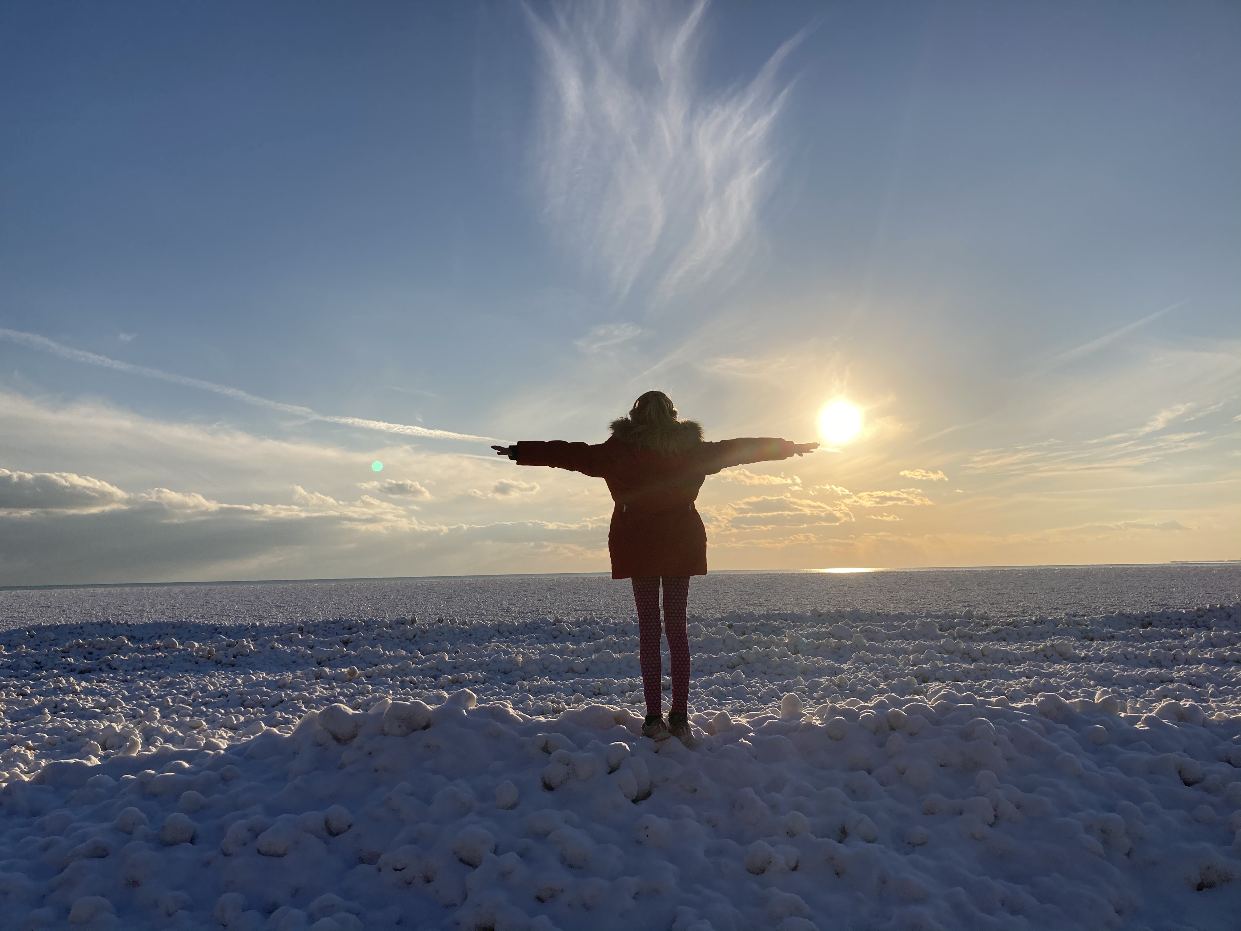 A woman stands with arms outstretched in front of a frozen lake