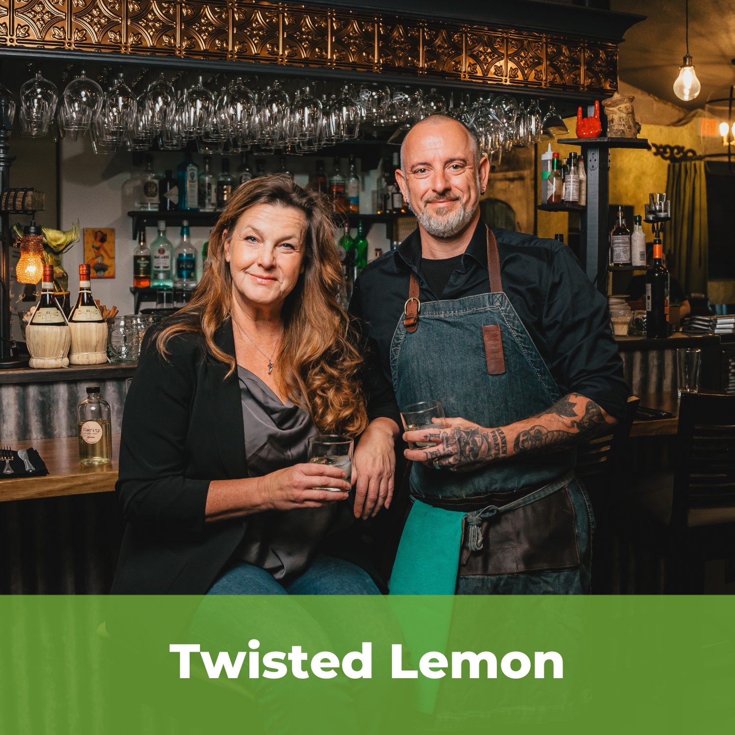Owners of Twisted Lemon standing in a dark room in front of a bar